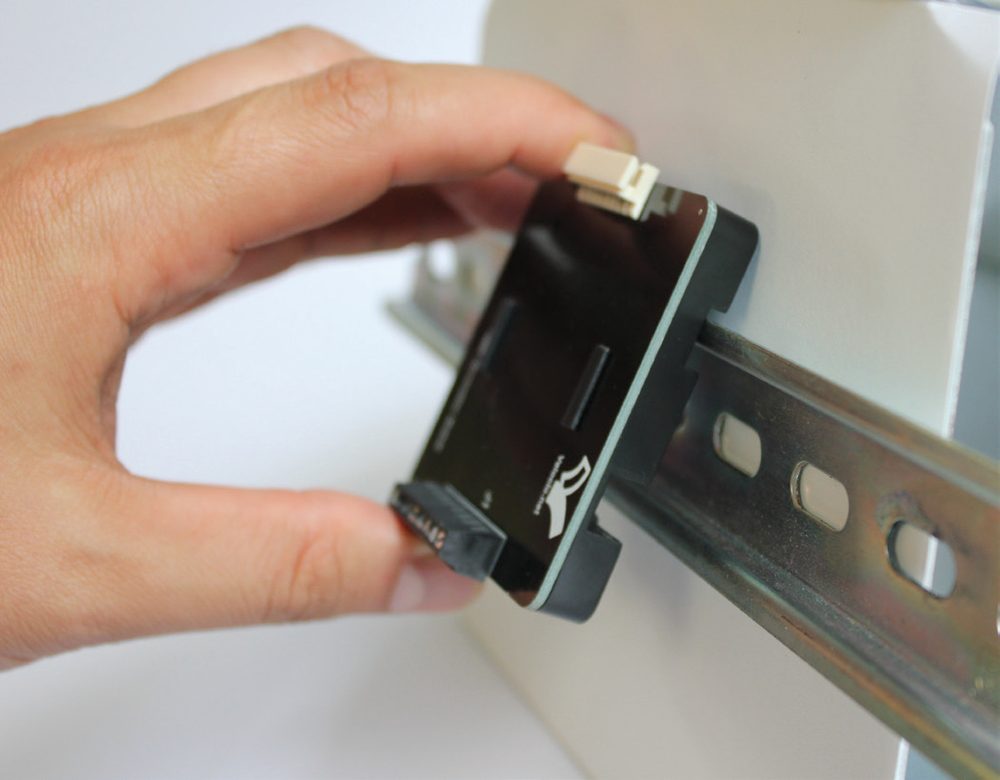 Hand resting the top edge of a TB06 terminal board clip onto a 35 mm DIN rail