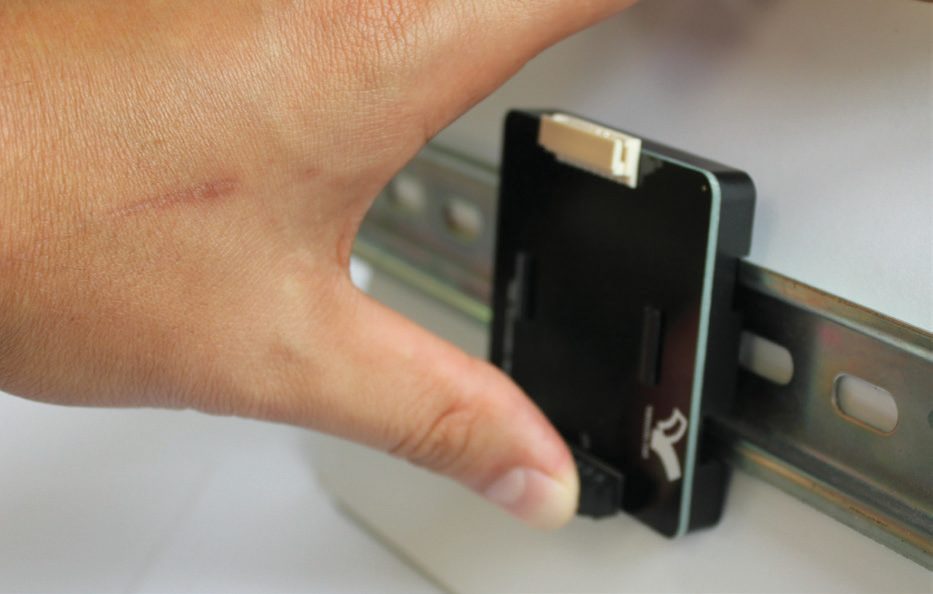 Thumb pressing the bottom end of a TB06 terminal board until the DIN rail clip snaps closed